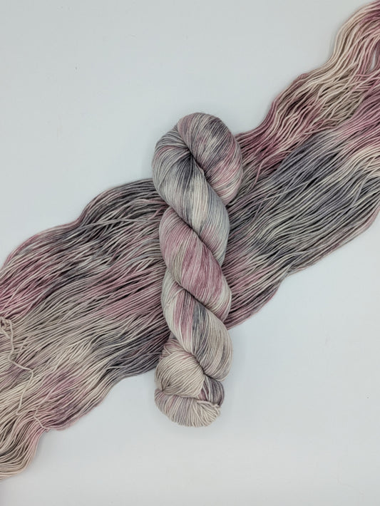 Ballet Slippers skein of fingering weight yarn on a skein spread out showing the pinks, grays, and white colors of the skein.