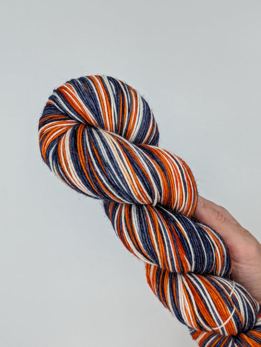 Blue, Orange, and White skein of yarn held against a plain background