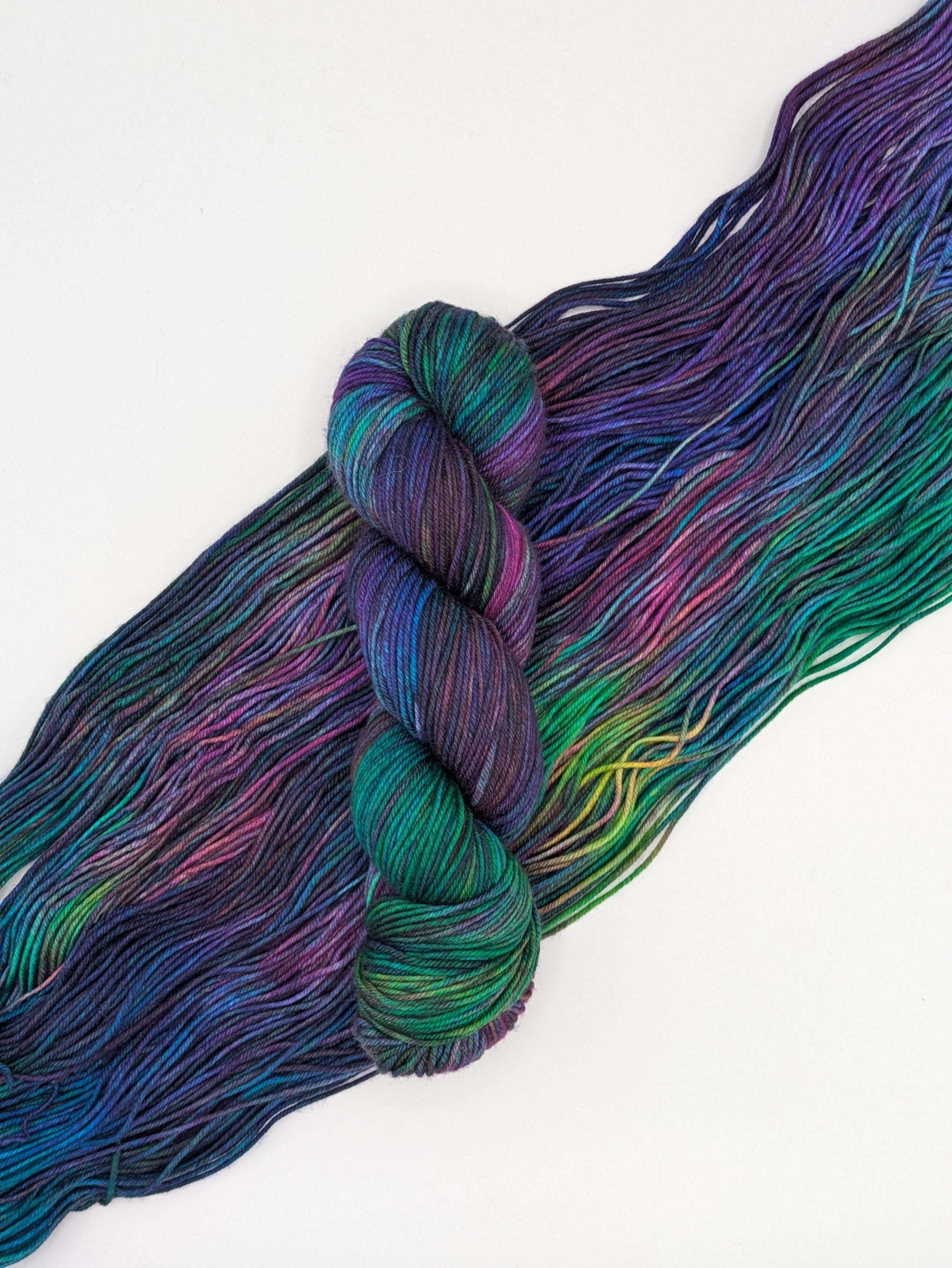 A skein of Galaxy DK weight yarn laying on a skein spread out to show it's jewel toned colors including blues, green, purples, greens.