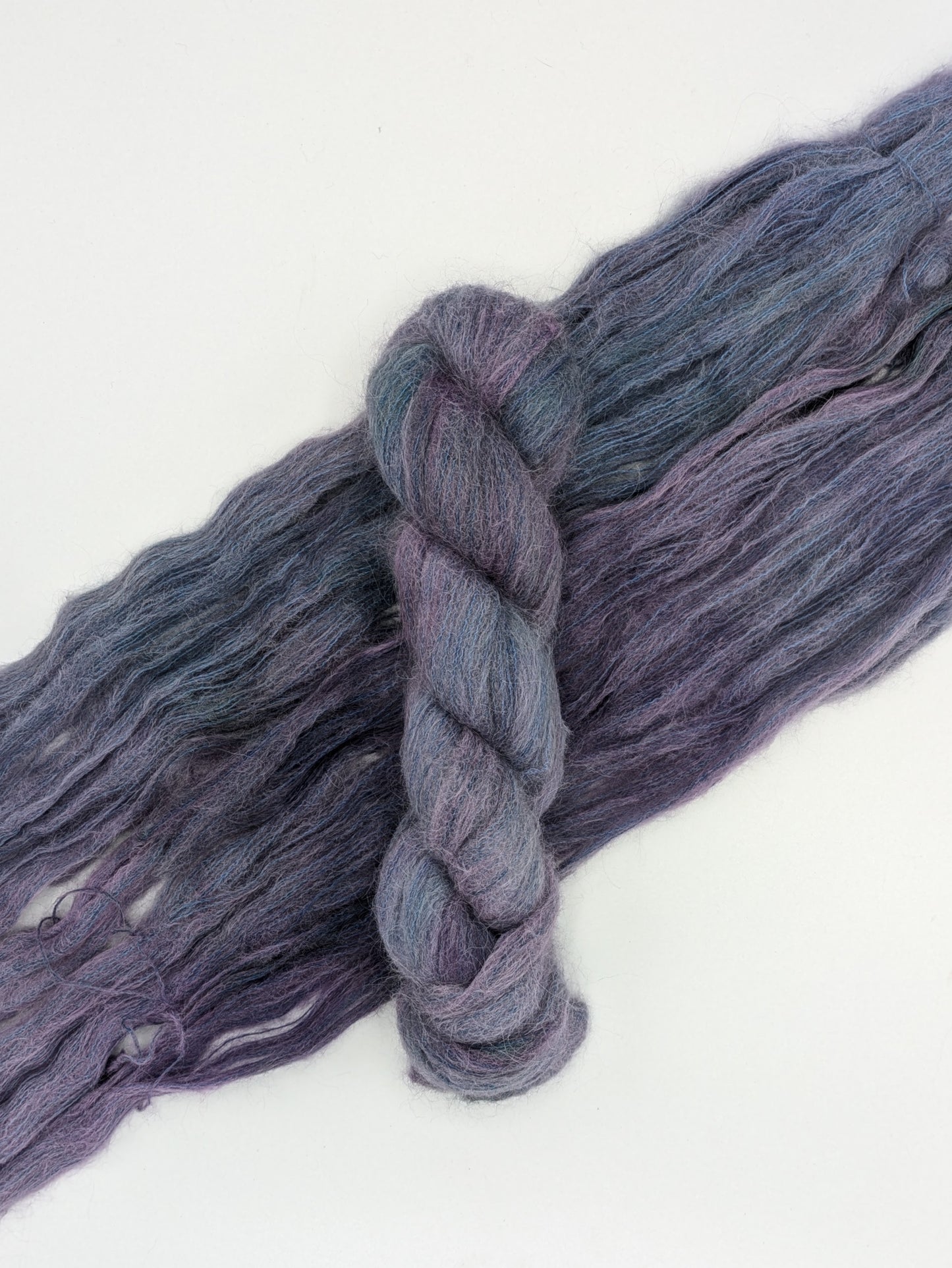 A skein of Galaxy suri silk yarn laying on a skein spread out to show it's blue and purple colors.