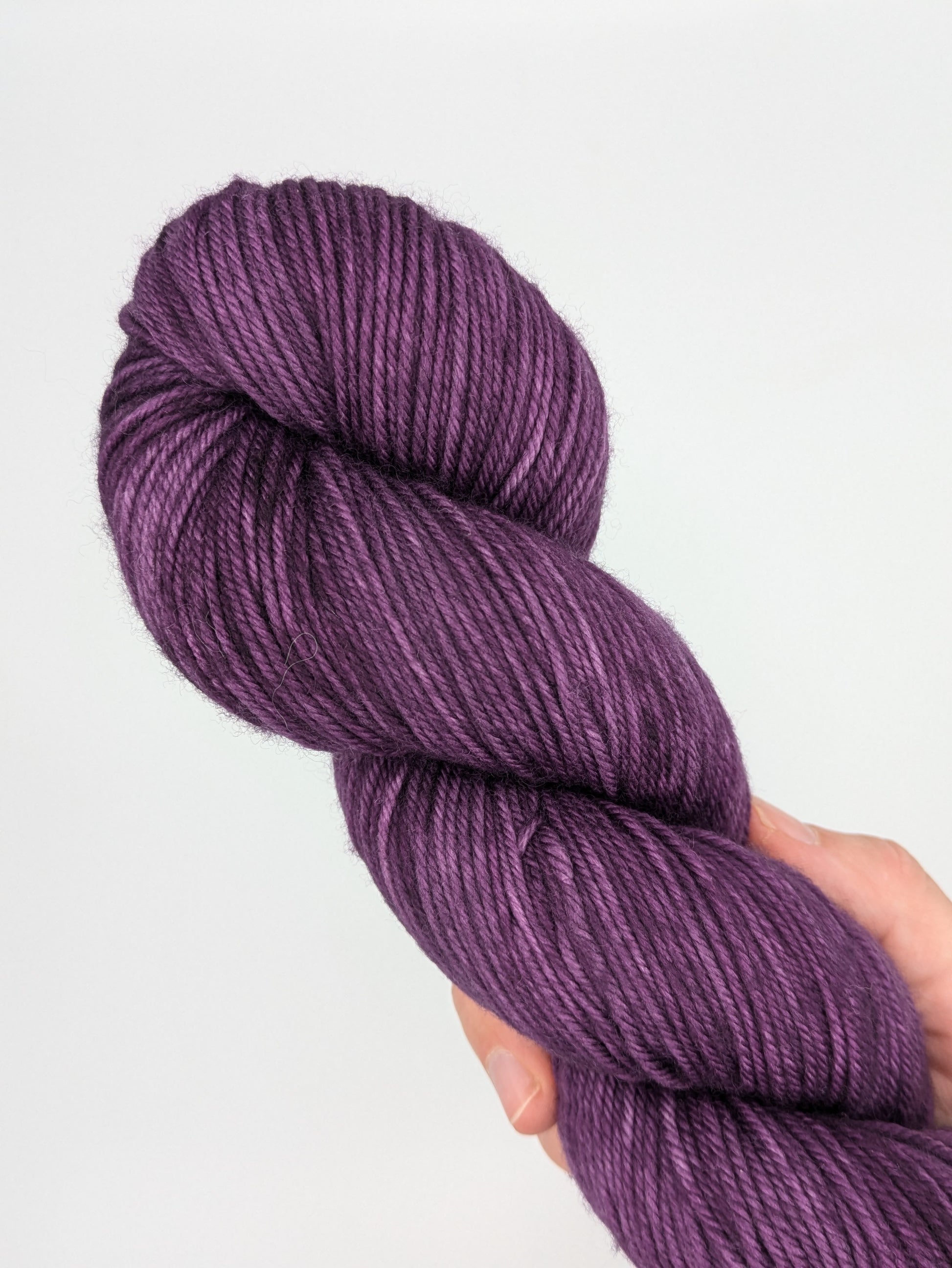 A hand holding a skein of Grape Jam DK weight yarn, showcasing a bright purple color