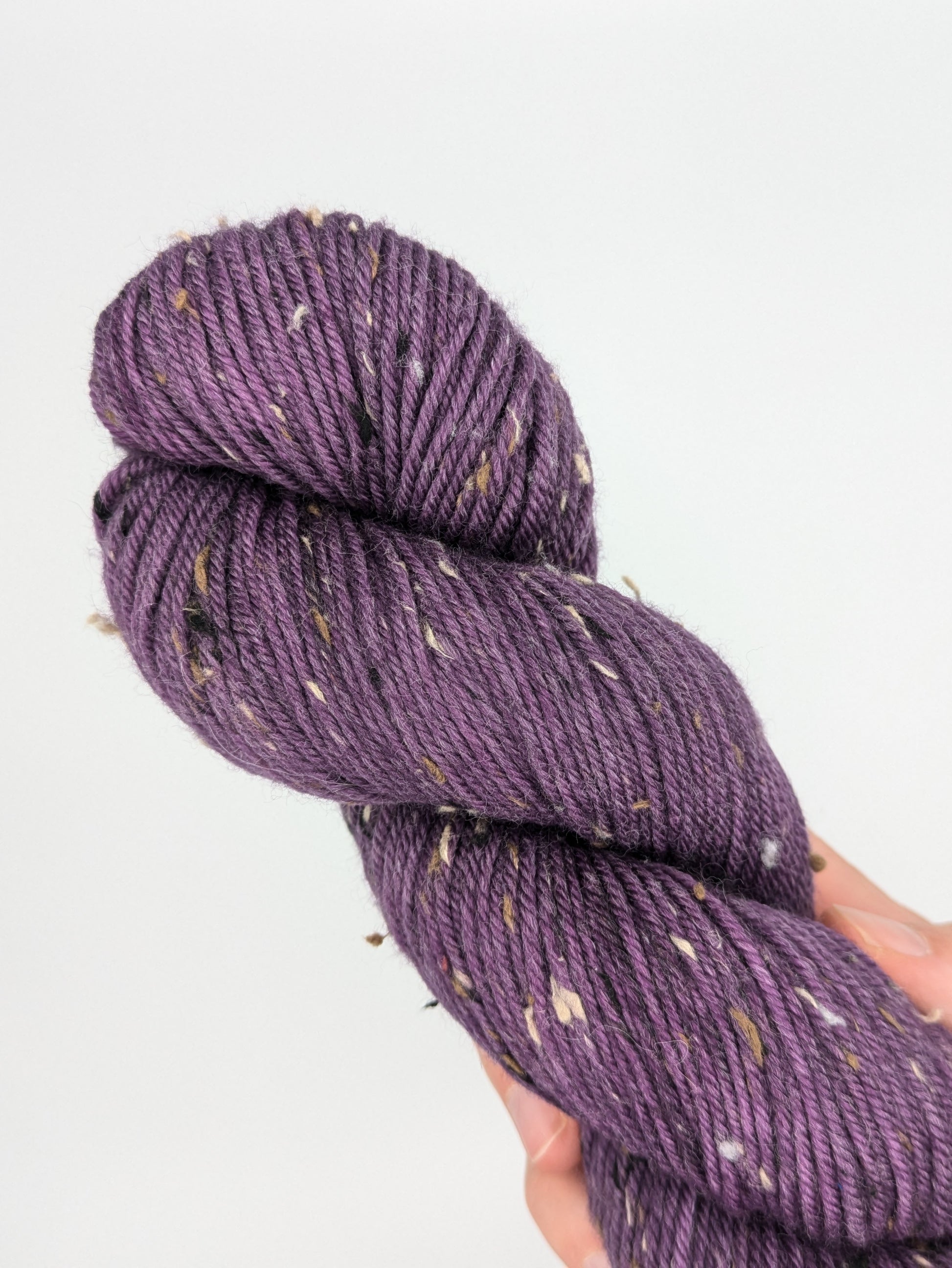 A hand holding a skein of Grape Jam Tweed DK weight yarn, showcasing a bright purple color