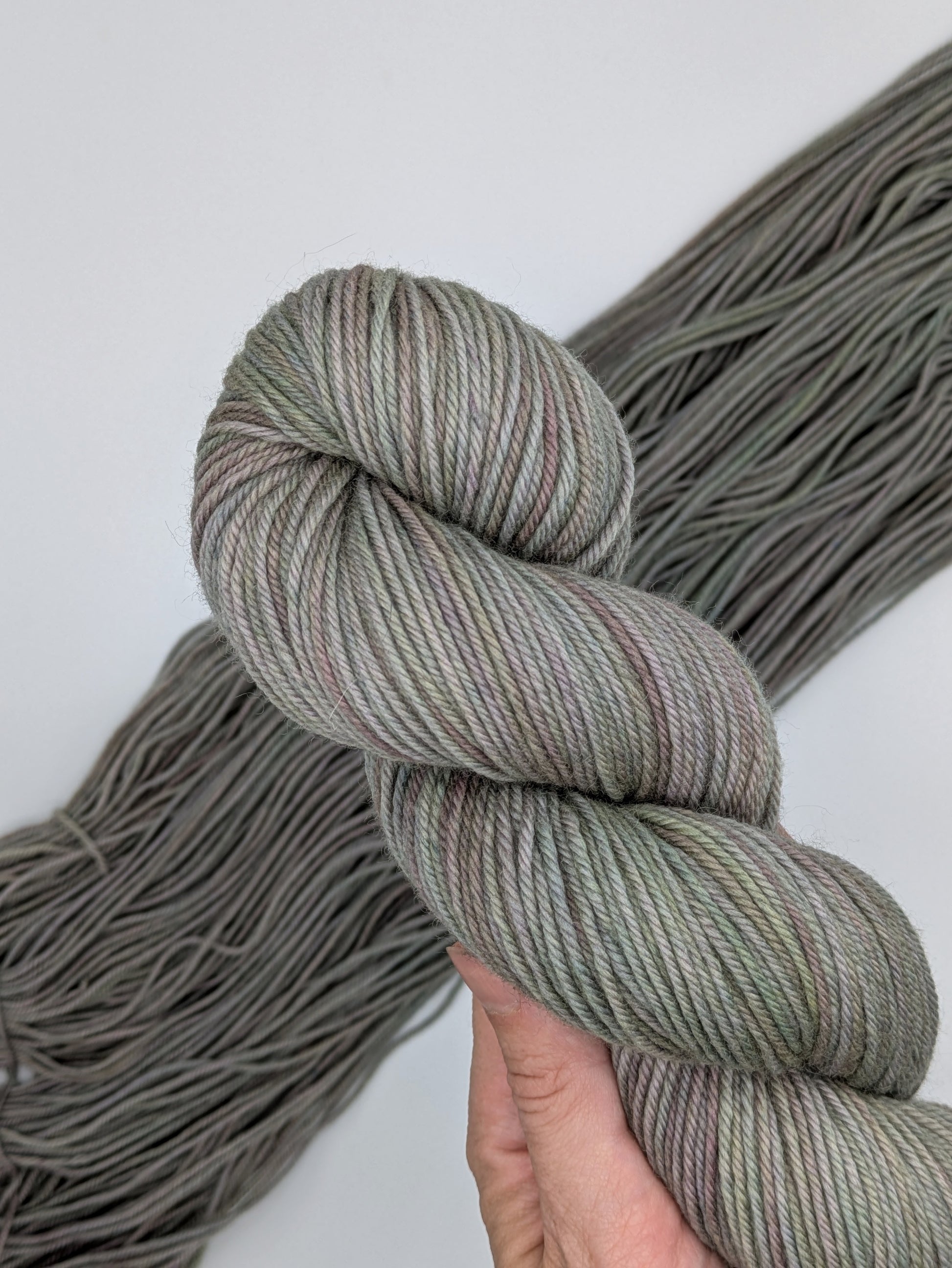 Mudbath Non-Superwash Yarn skein in DK weight, showing a slightly variegated green brown neutral color